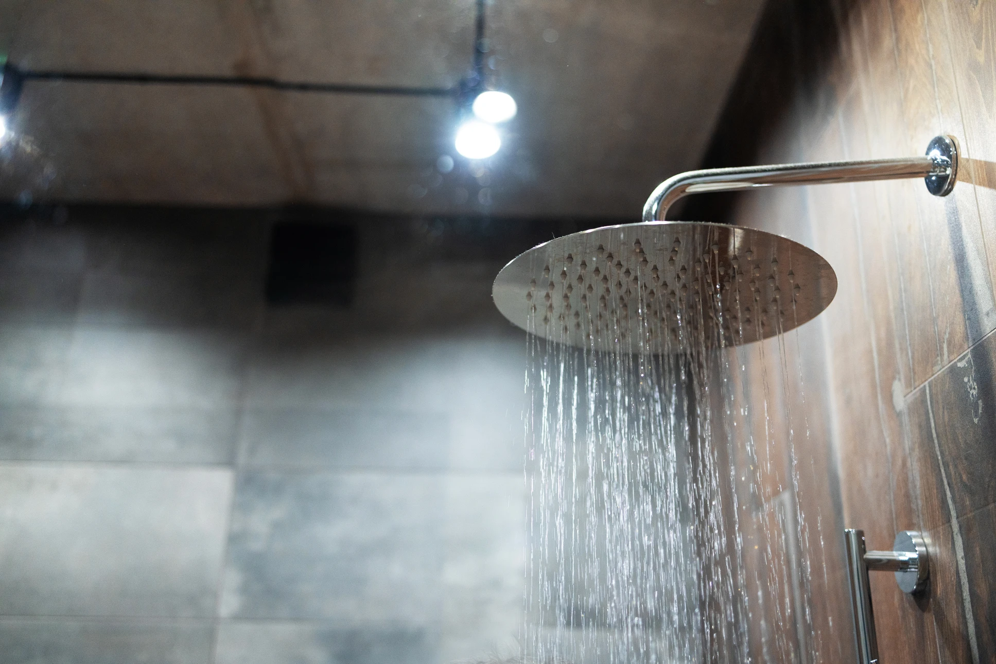 Intérieur de salle de bain avec pomme de douche chromée en fonctionnement, jets d'eau multiples créant des gouttelettes scintillantes sur fond bleu lumineux